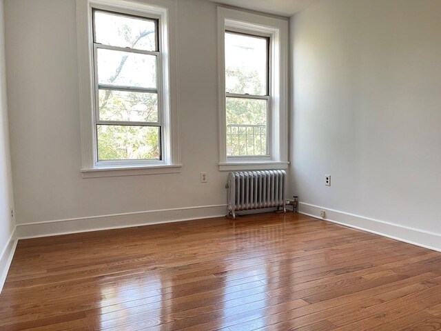 empty room featuring radiator heating unit, baseboards, and wood-type flooring