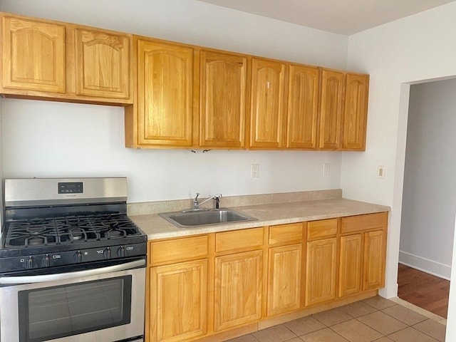 kitchen featuring a sink, gas stove, light countertops, light tile patterned floors, and baseboards