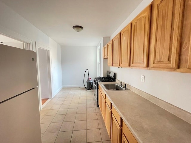 kitchen featuring stainless steel range with gas stovetop, light countertops, freestanding refrigerator, light tile patterned flooring, and a sink