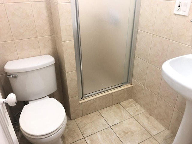 bathroom with tile patterned floors, toilet, a stall shower, and tile walls