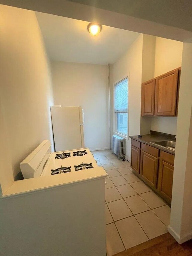 23-12 Broadway, Astoria, NY 11106 - kitchen with light tile patterned floors, radiator, freestanding refrigerator, a sink, and dark countertops
