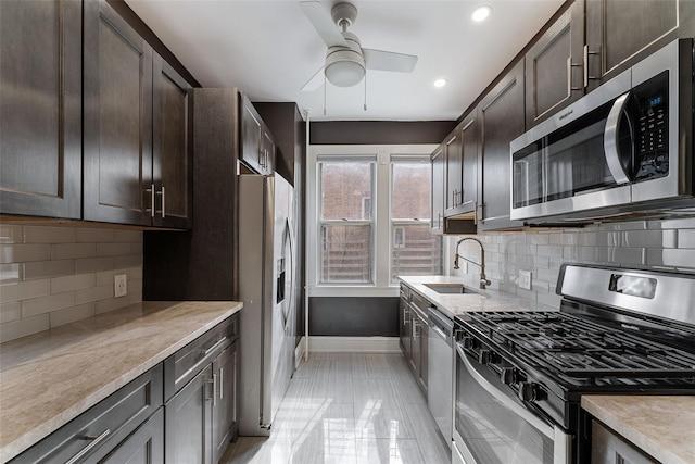 kitchen with a sink, appliances with stainless steel finishes, light countertops, baseboards, and dark brown cabinets