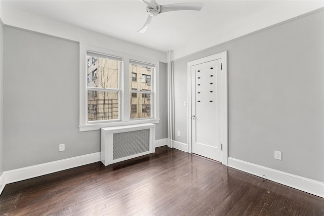 spare room featuring a ceiling fan, radiator, wood finished floors, and baseboards