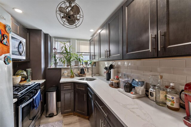 kitchen with light stone counters, dark brown cabinetry, appliances with stainless steel finishes, and a sink