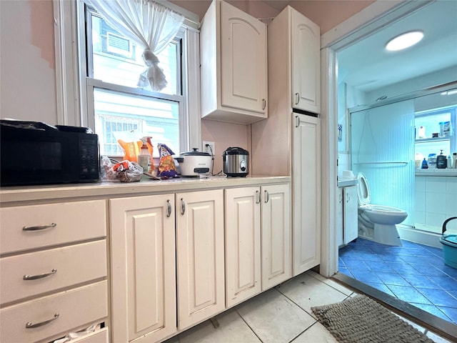 kitchen featuring light countertops, white cabinets, light tile patterned flooring, and black microwave