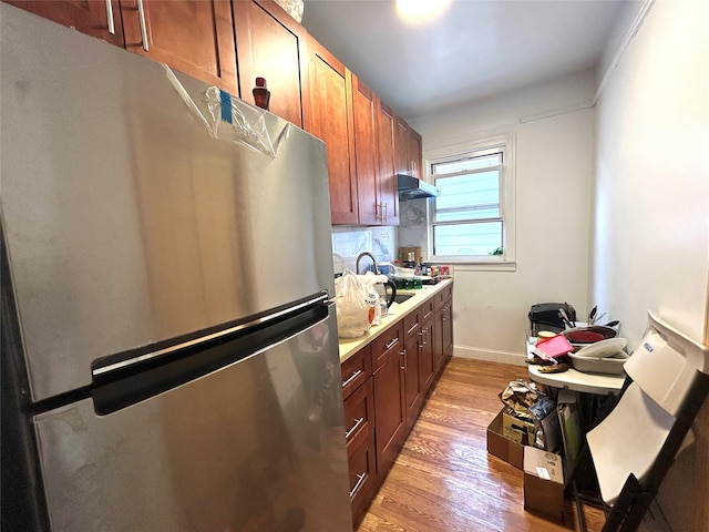 kitchen with light wood finished floors, baseboards, under cabinet range hood, freestanding refrigerator, and a sink