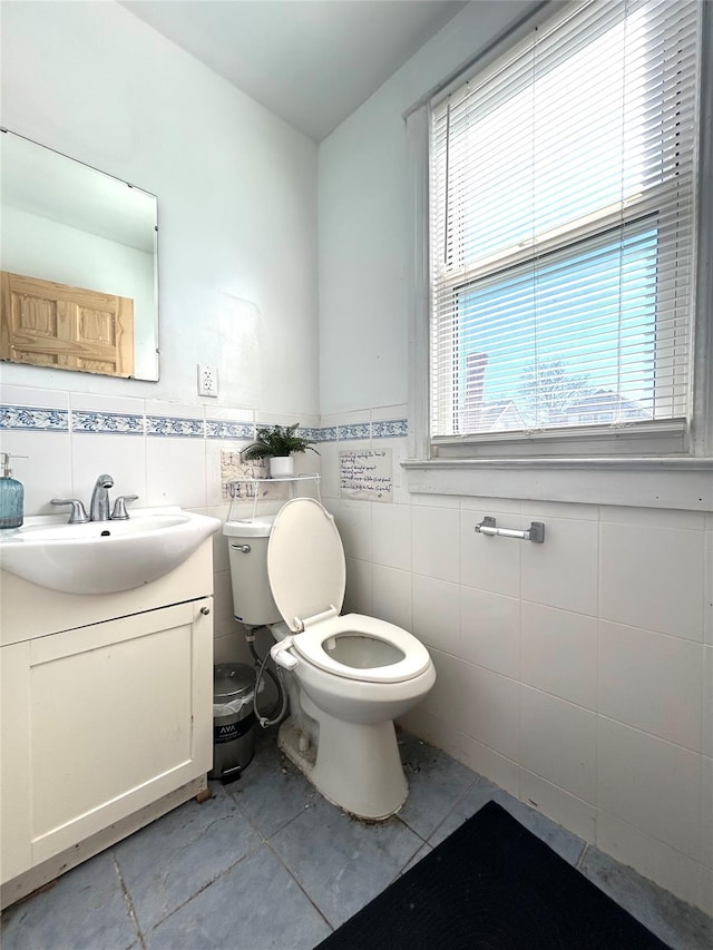 half bathroom featuring vanity, tile walls, toilet, and wainscoting