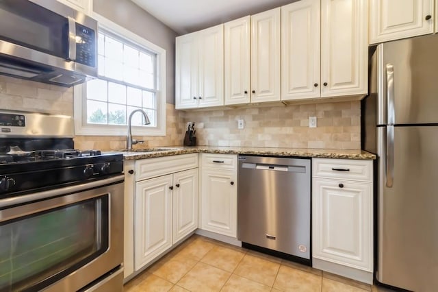 kitchen featuring light stone countertops, white cabinetry, a sink, light tile patterned floors, and stainless steel appliances