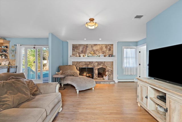 living room with a stone fireplace, visible vents, light wood finished floors, and a baseboard radiator