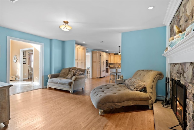 living room with light wood finished floors, baseboards, baseboard heating, recessed lighting, and a stone fireplace