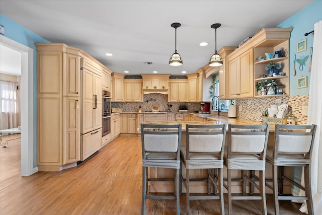 kitchen featuring light brown cabinets, a peninsula, a kitchen breakfast bar, and a sink