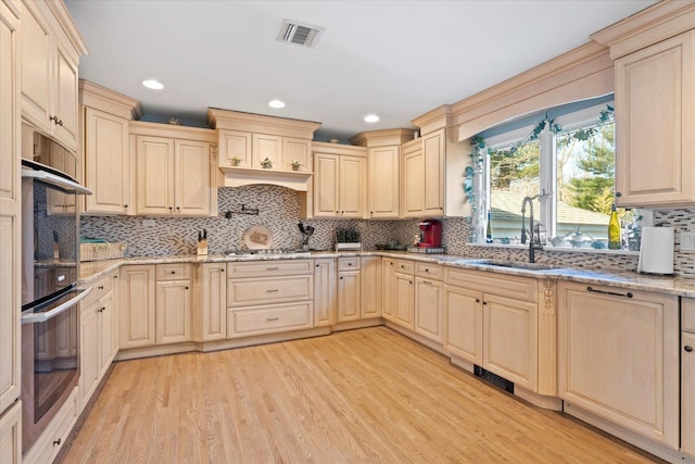 kitchen with light stone countertops, visible vents, a sink, stainless steel appliances, and light wood-type flooring