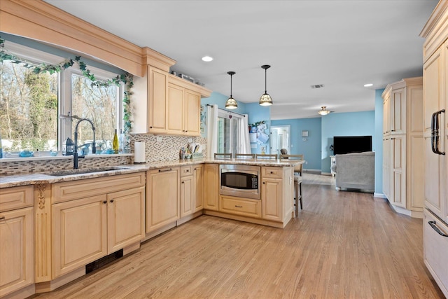 kitchen with stainless steel microwave, light brown cabinets, open floor plan, a peninsula, and a sink