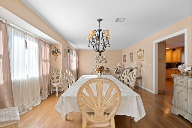 dining space featuring an inviting chandelier, wood finished floors, visible vents, and baseboards