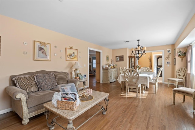 living room featuring visible vents, wood finished floors, baseboards, and a chandelier