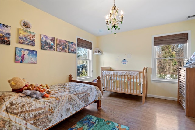 bedroom with a notable chandelier, multiple windows, visible vents, and wood finished floors