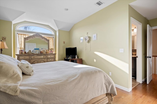 bedroom with visible vents, wood finished floors, baseboards, and vaulted ceiling