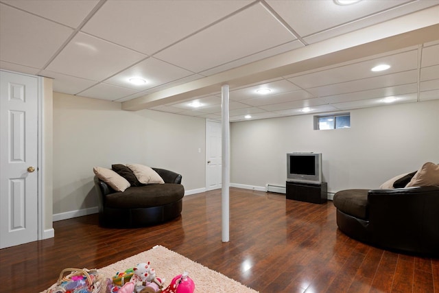 living room featuring baseboard heating, a drop ceiling, baseboards, and wood finished floors