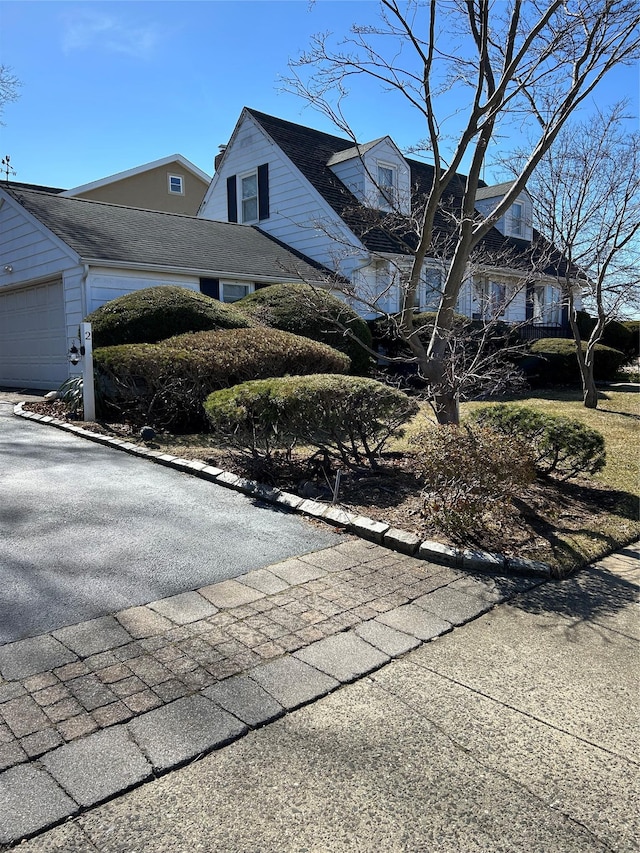 view of side of property with a garage, roof with shingles, and aphalt driveway