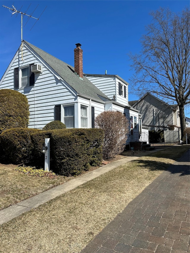 view of home's exterior featuring an AC wall unit, a chimney, and roof with shingles