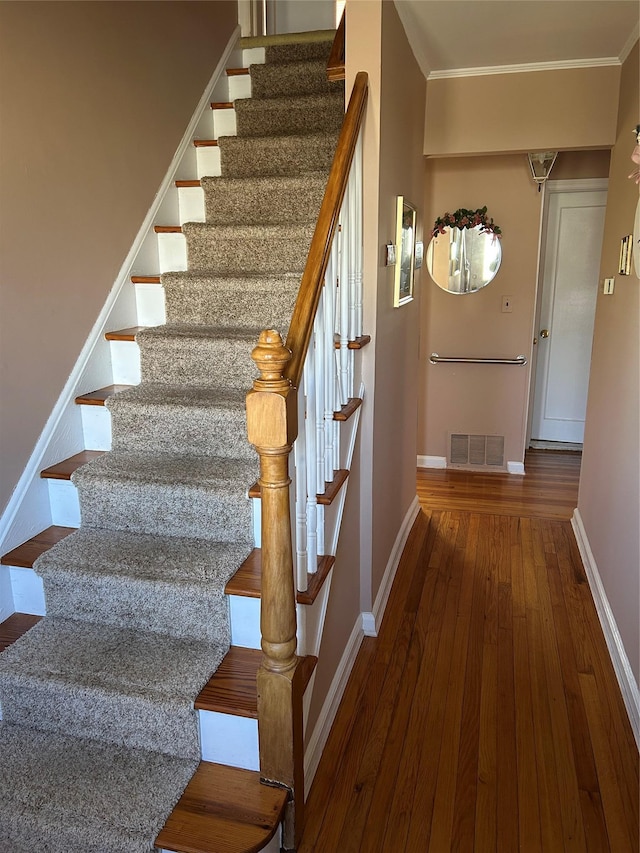 stairway featuring visible vents, wood-type flooring, baseboards, and crown molding