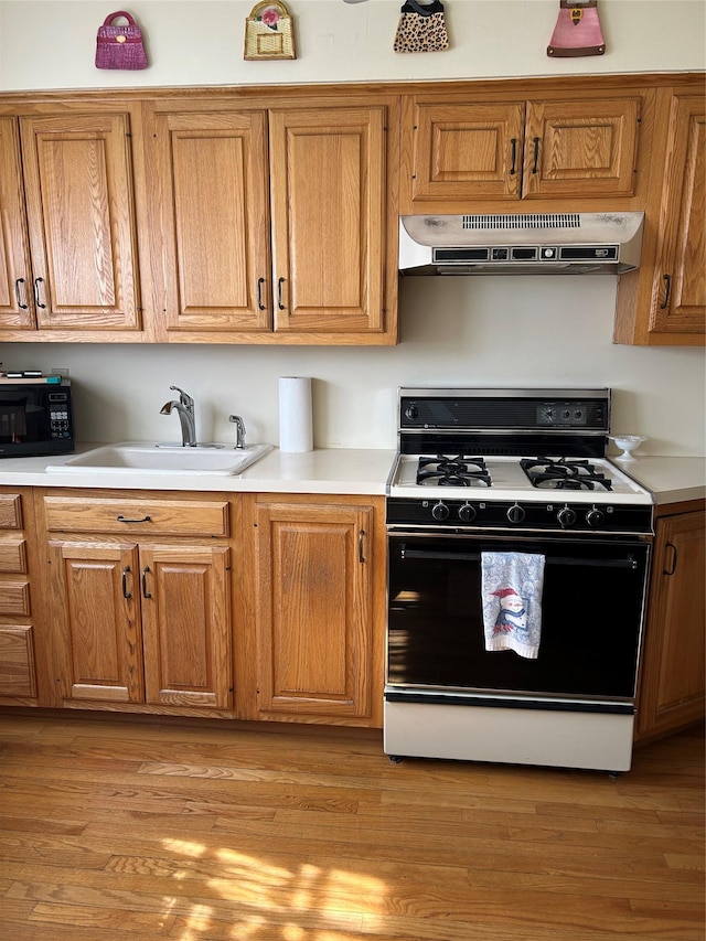 kitchen with black microwave, under cabinet range hood, light wood-type flooring, gas stove, and a sink