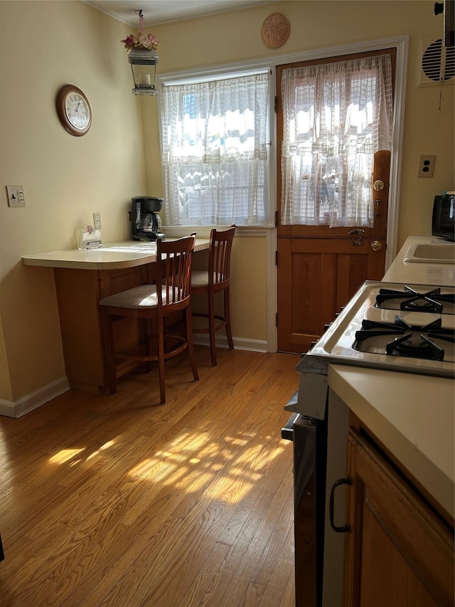 kitchen featuring baseboards, range with gas stovetop, light wood-style floors, and light countertops