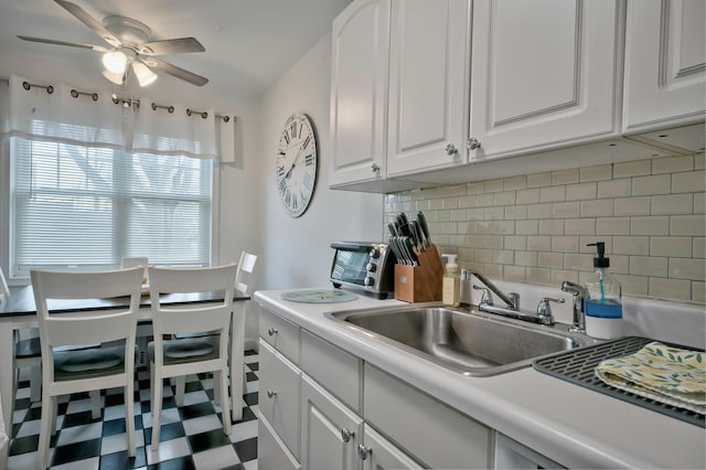 kitchen with tasteful backsplash, light countertops, white cabinets, a ceiling fan, and a sink