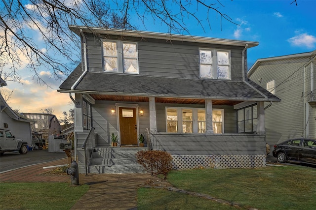 view of front of home featuring a porch, a shingled roof, and a front lawn