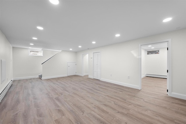 finished basement featuring light wood-style flooring, recessed lighting, stairway, a baseboard radiator, and baseboards