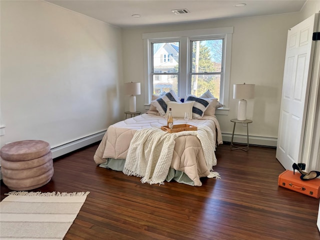 bedroom with baseboard heating, baseboards, visible vents, and wood finished floors