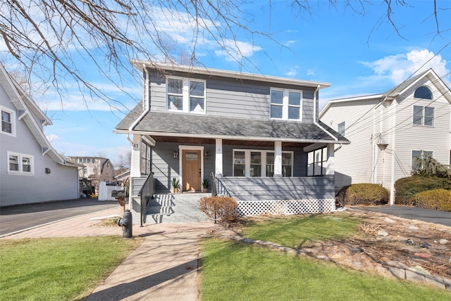 view of front of property featuring a front yard, covered porch, and a shingled roof