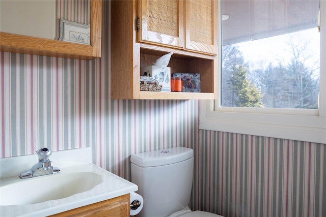 bathroom with toilet, wallpapered walls, and vanity