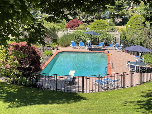 community pool with a patio, a lawn, and fence