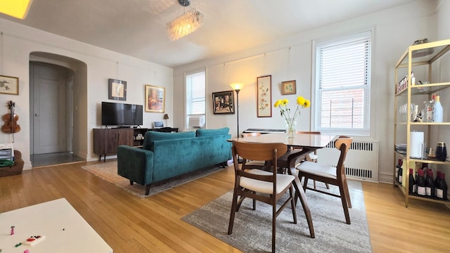 dining area with arched walkways, plenty of natural light, radiator heating unit, and light wood finished floors