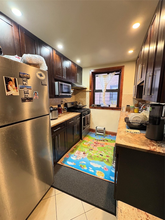 kitchen featuring under cabinet range hood, backsplash, stainless steel appliances, dark brown cabinetry, and light tile patterned floors