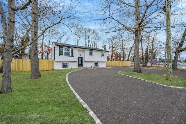 split foyer home featuring aphalt driveway, fence, a front yard, and a chimney