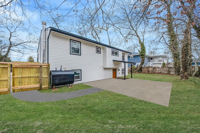 rear view of house with heating fuel, fence, a yard, a chimney, and a patio area