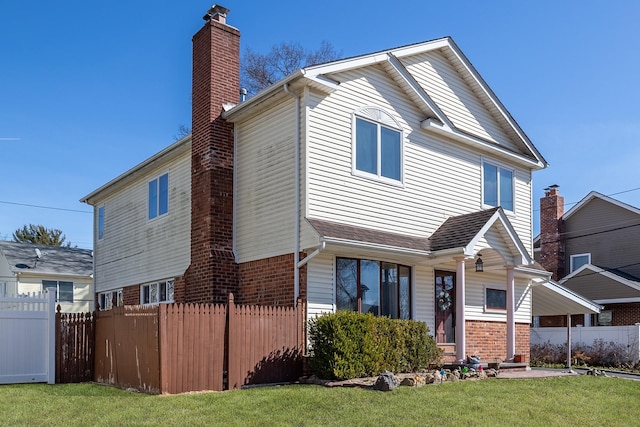 rear view of house featuring a yard, brick siding, a chimney, and fence