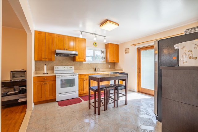 kitchen featuring freestanding refrigerator, decorative backsplash, light countertops, under cabinet range hood, and white electric range