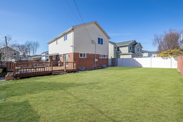 rear view of property featuring a deck, fence, brick siding, and a lawn