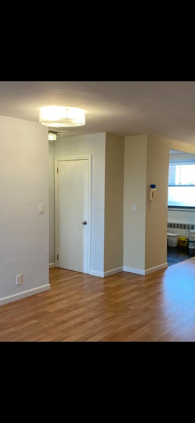 empty room featuring baseboards, radiator, and light wood finished floors