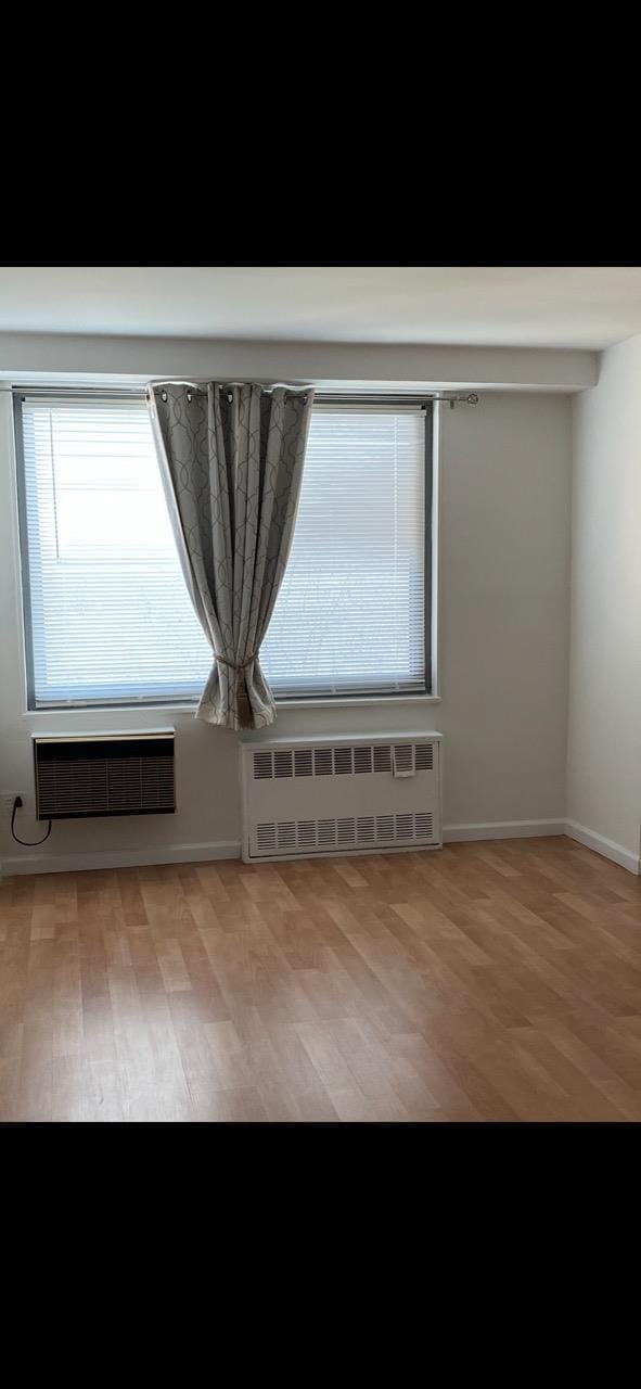 empty room featuring radiator, a wall mounted air conditioner, baseboards, and wood finished floors