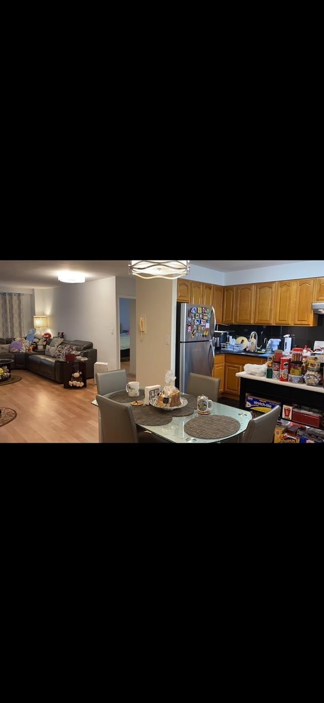 interior space featuring light brown cabinetry, freestanding refrigerator, under cabinet range hood, and wood finished floors