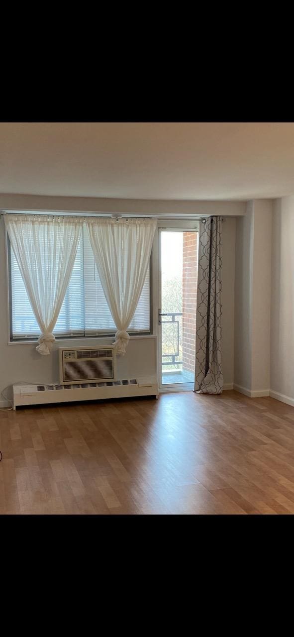 unfurnished room with light wood-style flooring, baseboards, baseboard heating, and a wall mounted AC