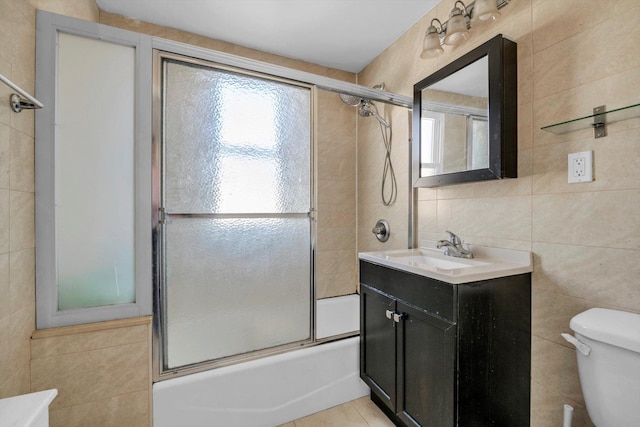 bathroom featuring combined bath / shower with glass door, toilet, tile walls, and vanity