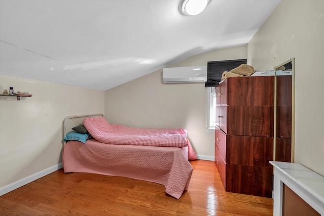 bedroom with vaulted ceiling, light wood-style flooring, baseboards, and a wall mounted air conditioner