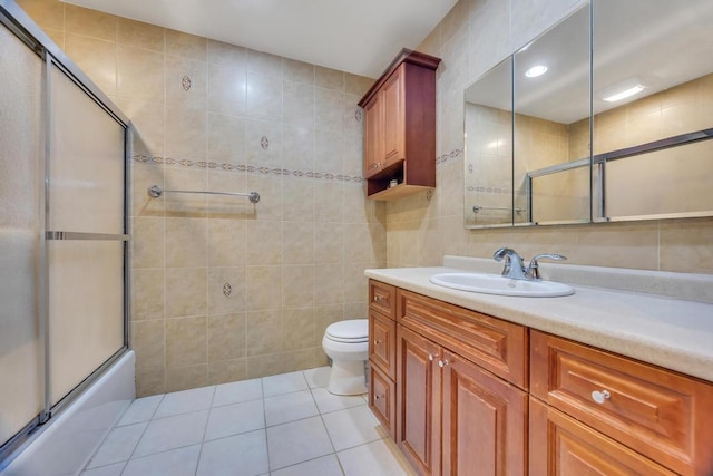 bathroom with tile patterned flooring, toilet, vanity, combined bath / shower with glass door, and tile walls