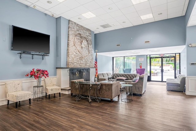 living area with visible vents, a drop ceiling, a towering ceiling, and wood finished floors