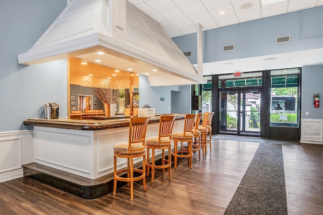 bar featuring a community bar, visible vents, a towering ceiling, and a wainscoted wall